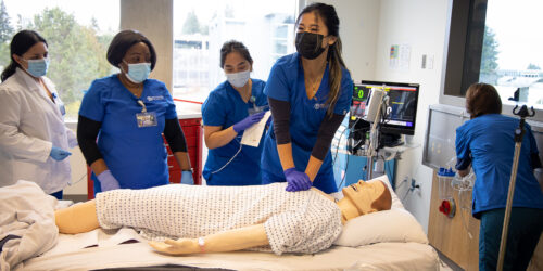 A woman performing CPR on a dummy in front of a class