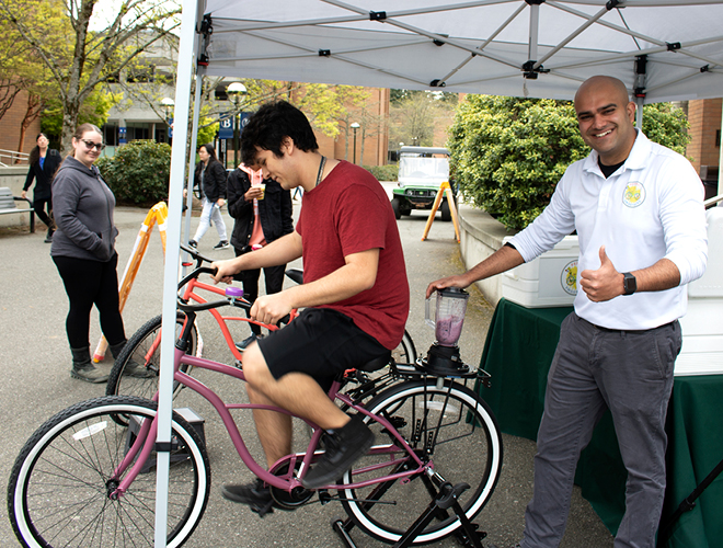 A student demonstrates how to blend a drink by riding a bike at a tent on BC's campus.