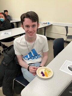 An OLS student sitting in classroom with a paper plate filled with veggies.