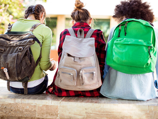 Three students with backpacks sit side-by-side on campus.