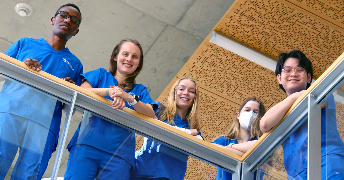 Students in scrubs lean over a campus balcony.