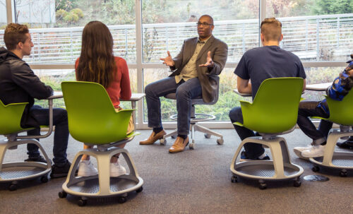 A professor sitting with students in a relaxed setting