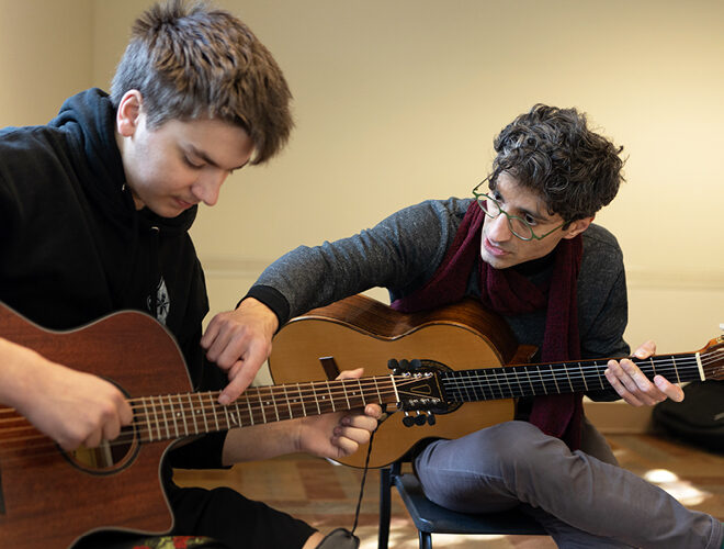 A music professor demonstrates finger placement and chords on a guitar.