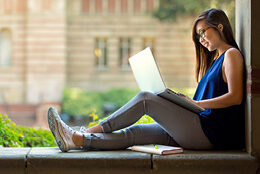 A student studies on a laptop in a campus quad.