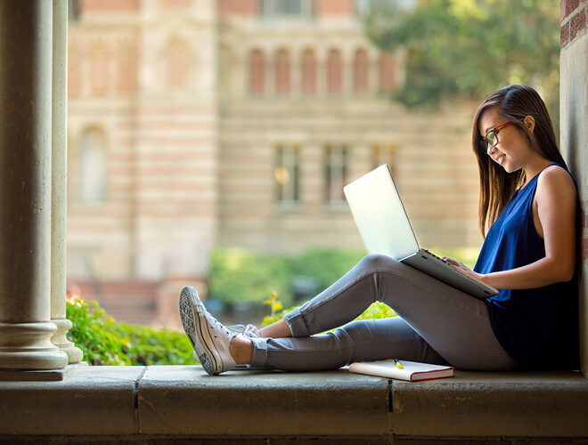 A student works on a laptop on a campus quad.