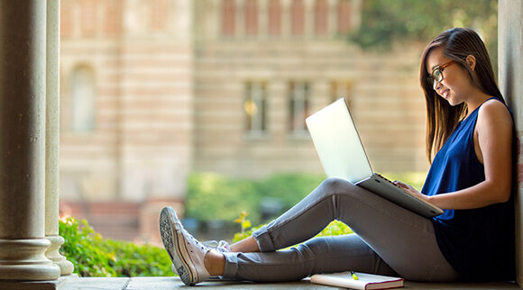 A student works on a laptop on a campus quad.