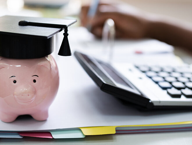 A piggybank with a graduation cap sits near a calculator and a school binder.