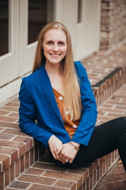 Woman sitting on brick stairs smiling and wearing a blue jacket.