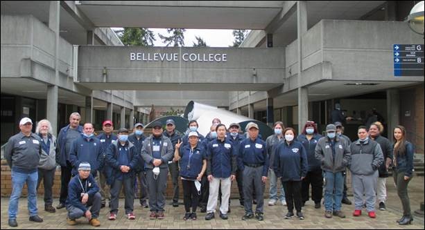 Custodial crew gathers in the courtyard beneath the words "Bellevue College" to pose by the fountain.