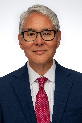 A smiling man with black glasses wearing a blue suit, white shirt, and red tie.