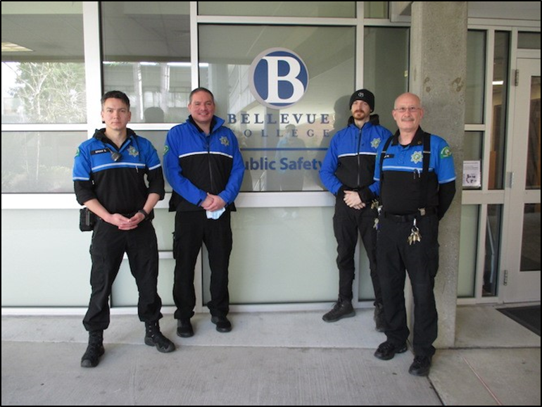 Four public safety staff and officers wearing black and blue uniforms standing in front of the windows of the Public Safety Office.