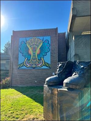 A vibrant and intricate mural, Indigena por Vida, overlooks a sunny, grassy hill with clear blue skies above.