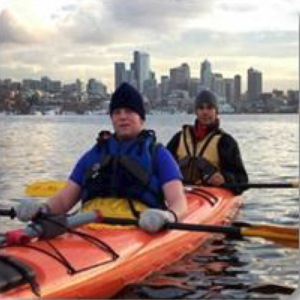 Two BC students kayaking in Puget Sound with Seattle skyline in the background.