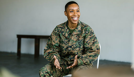 Woman in green and brown camouflage uniform smiling explaining her thoughts.