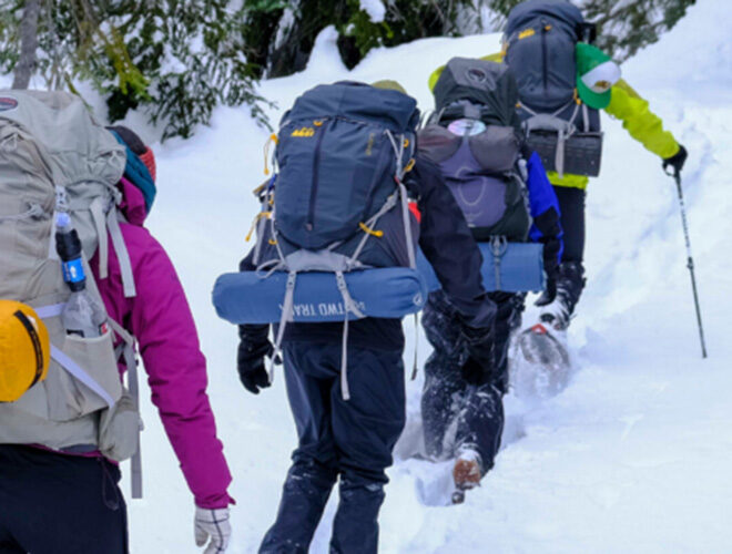 Snowshoe hikers with full packs and gear hiking through the forest