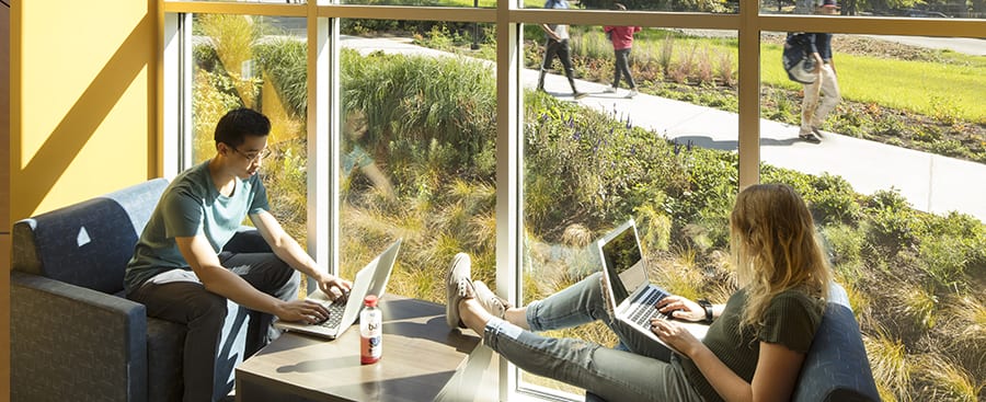 Students with their laptops sitting in a corner window.