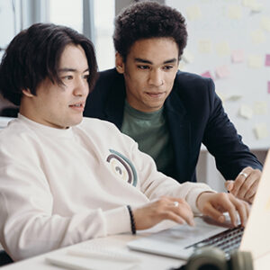 Two professionals discuss while working on a laptop.