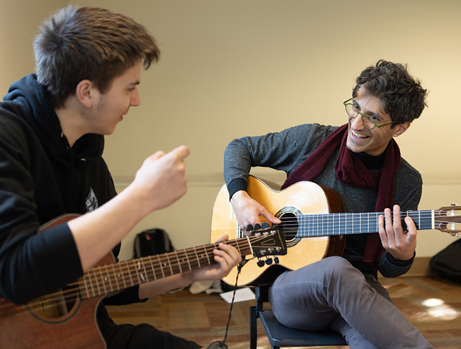 A music professor demonstrates playing the guitar for a student.