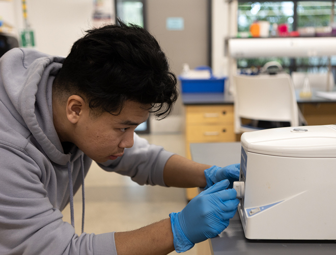 A student in a lab wearing blue gloves making adjustments to a lab experiment.