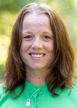 Alicia smiling with a blurred green background and a silver lock necklace