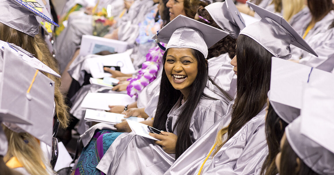 A BC graduate in cap and gown grins.