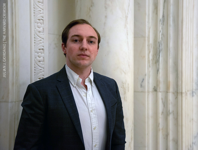 Quinn H.J. Ewanchyna standing in the Harvard University, Widener Library, wearing a dark blue blazer and white button-down shirt.