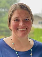 Dr. Chris smiling, wearing a long pearl necklace, a grassy landscape in the background