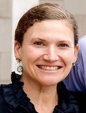 Deborah smiling, wearing a black ruffled blouse and round earrings