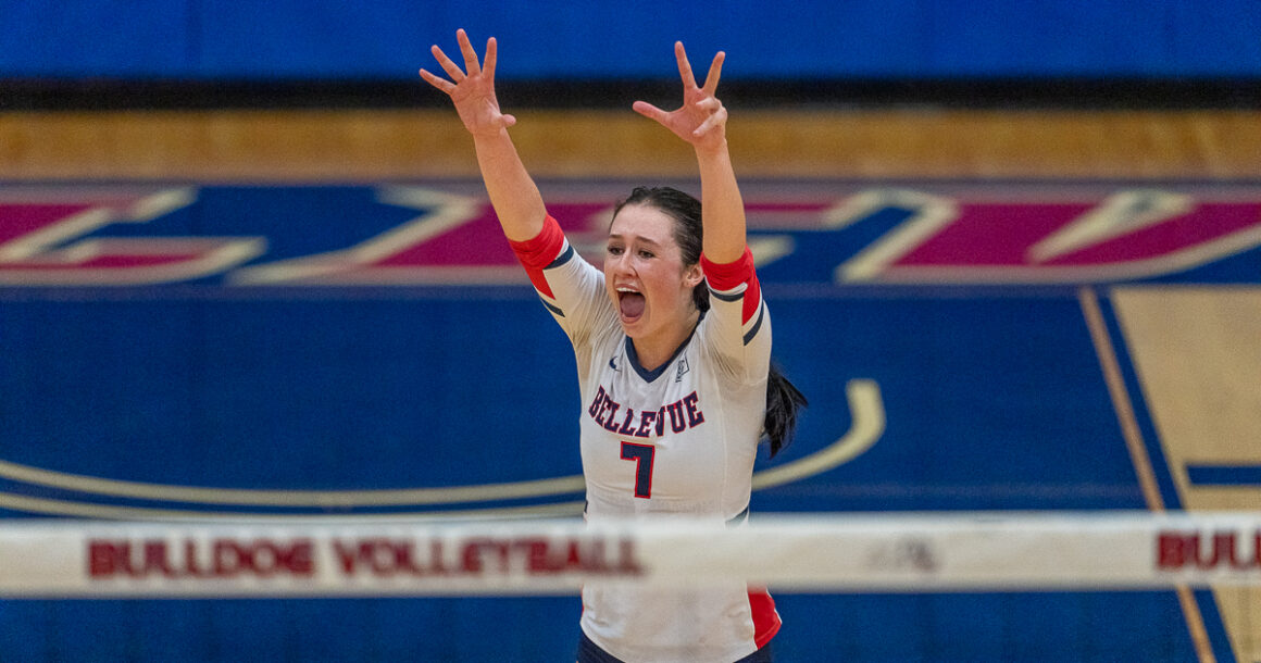 Marin Mackey stands in front of the volleyball net with her arms raised