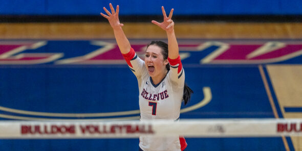 Marin Mackey stands in front of the volleyball net with her arms raised