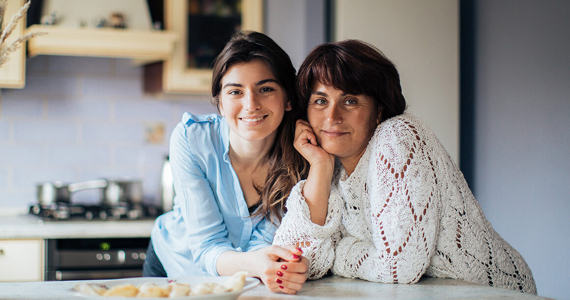 A parent and child smile together in their kitchen.