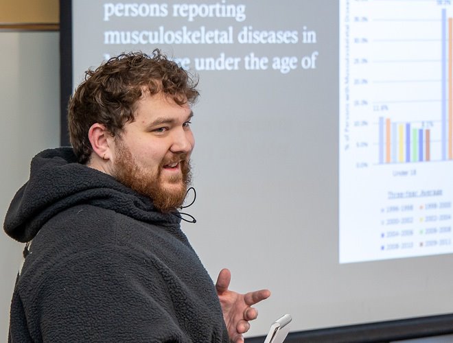 Faculty member in front of a projection screen giving a presentation about musculoskeletal diseases.