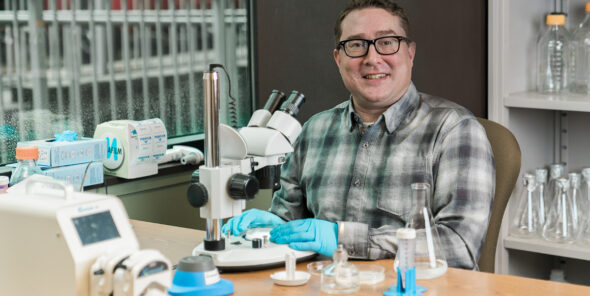 Bellevue College alum Michael Muir sits at a table with a microscope.