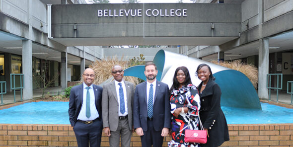 Four people pose for a photo in front of the Bellevue College fountain on campus.