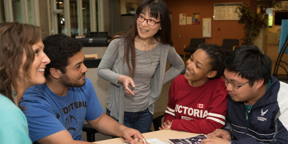 Five people, students and faculty, at a table, smiling.