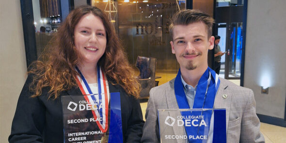 Two students smile and pose with their DECA nationals trophies.