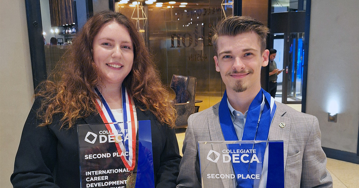 Two students smile and pose with their DECA nationals trophies.