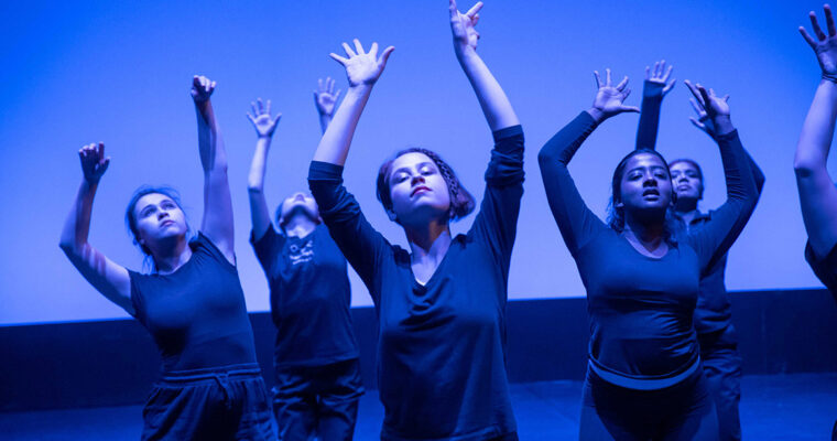 A group of four people hold their hands up as they close their eyes.