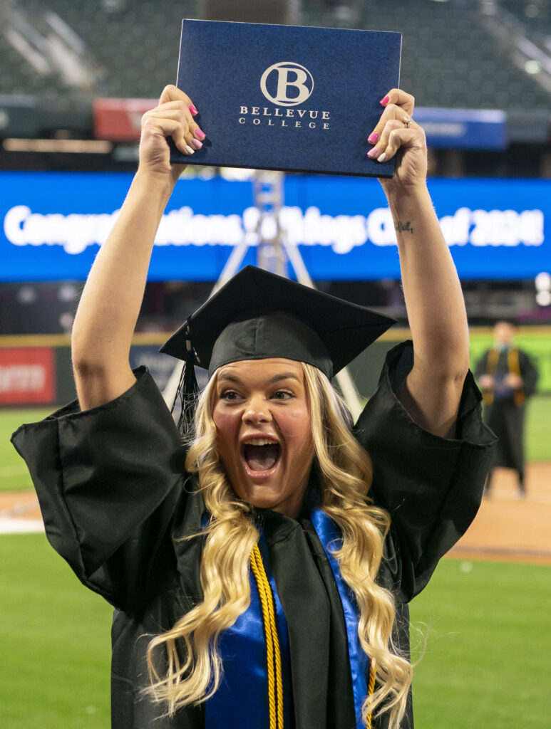 A BC graduate holds their diploma in the air at commencement.
