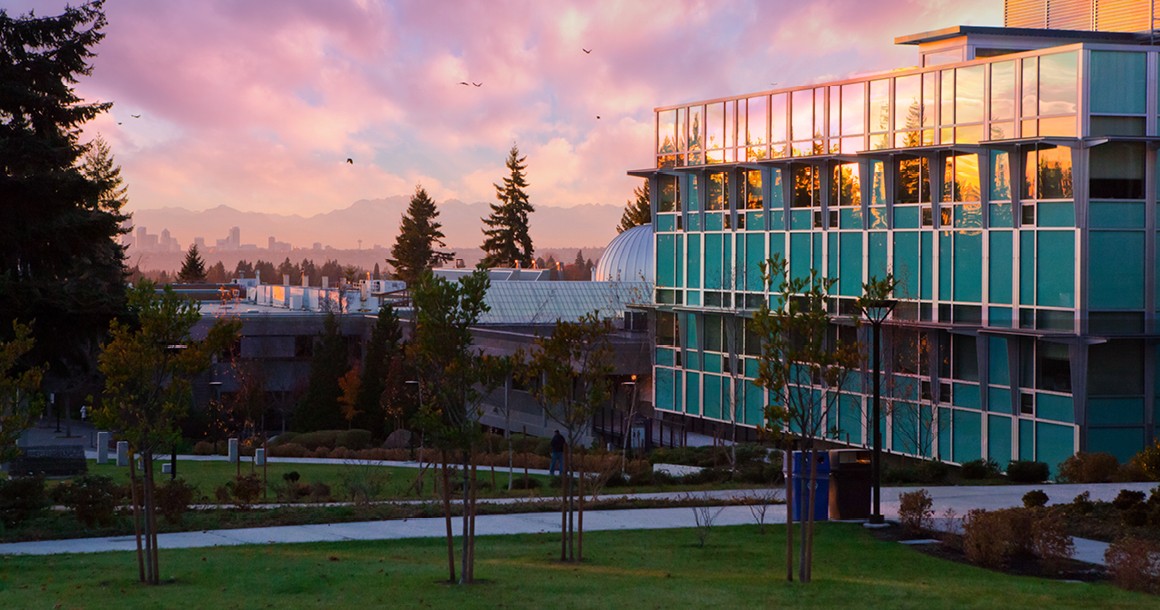 Bellevue College's science building is lit with sunlight and complemented by the city skyline.