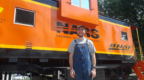 An OLS alum stands in front of a train at his workplace.
