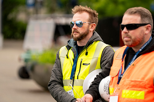 Two men wearing sunglasses and brightly colored vests stand at event.