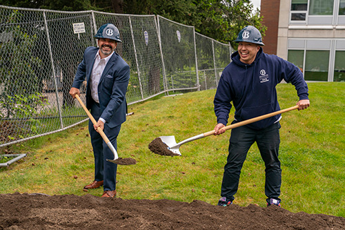 Two people pose with shovels and dirt.