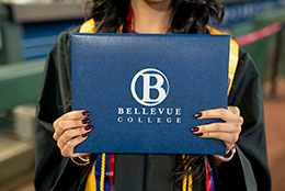 Bellevue College graduate holding diploma cover with Bellevue College logo on it