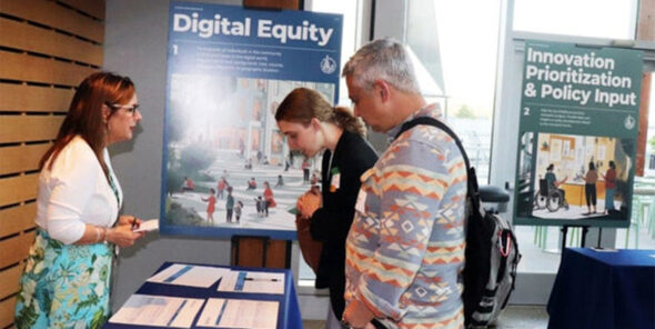 Three people talk at a table with resources and information featured.