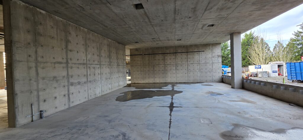 Space with cement floor, ceiling, and wall, and one open wall with a pillar. 