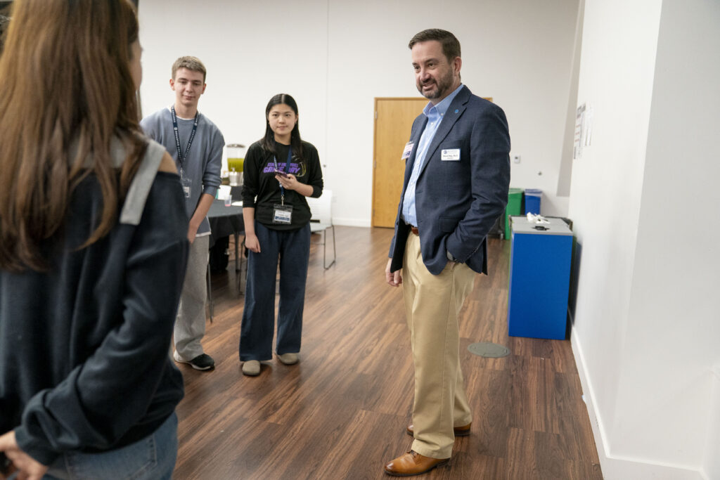 President David May speaks with several people while standing.