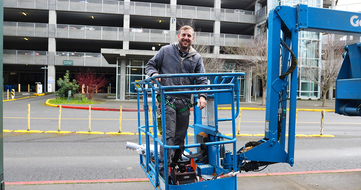 Person stands in the basket of a blue crane in front of the parking garage.