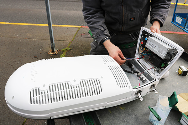 A person opens the back of a large, white street light head.