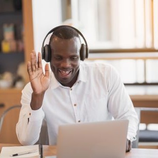 A man wearing headphones waves at his laptop during a meeting